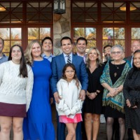 Victor Cardenas poses with large group of people outside of the Alumni House